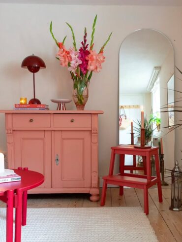 Balcão de madeira rosa com luminária e vaso de flores, e mesa de madeira bordô