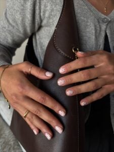 Mãos de pele clara, com anéis em dourado e unhas curtas com poá