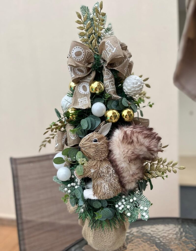 Pequena árvore de Natal decorado com bolas brancas e douradas, laços e um esquilo