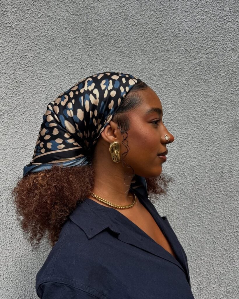 Mulher de pele preta, com blusa preta, acessórios em dourado e cabelo crespo com lenço