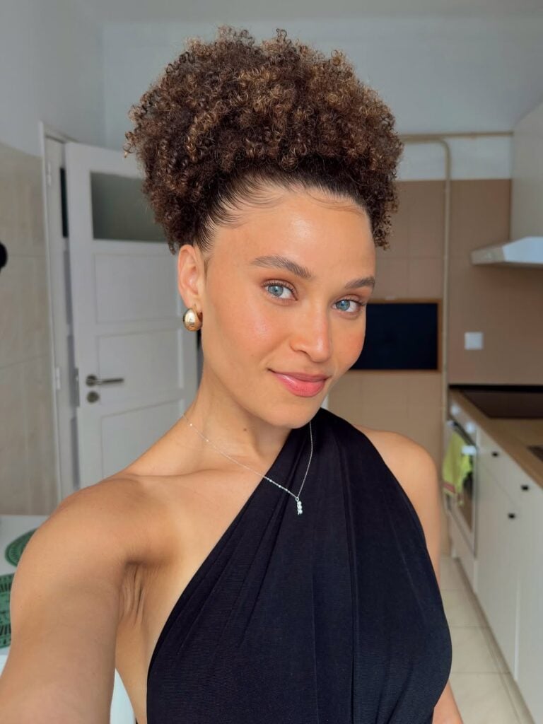 Mulher de pele clara, com roupa preta e cabelo crespo preso em coque