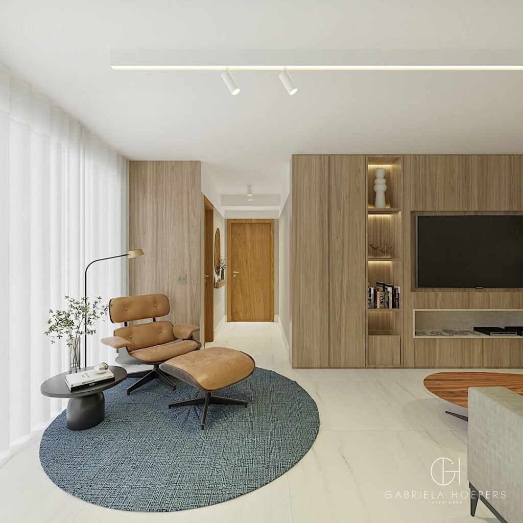Sala de estar com painel amadeirado, cantinho da leitura com tapete redondo cinza, poltrona de couro caramelo e luminária de piso