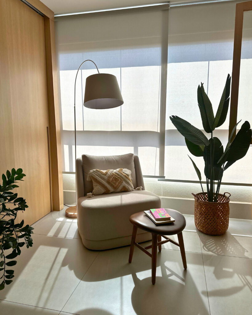 Cantinho da leitura iluminado com poltrona, luminária de piso e cesto com plantas