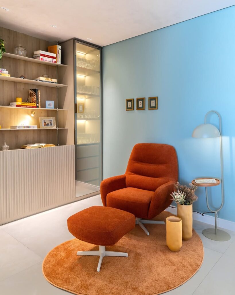 Ambiente com parede azul-claro, mesa e luminária integradas, poltrona com peseira estofada na cor terracota
