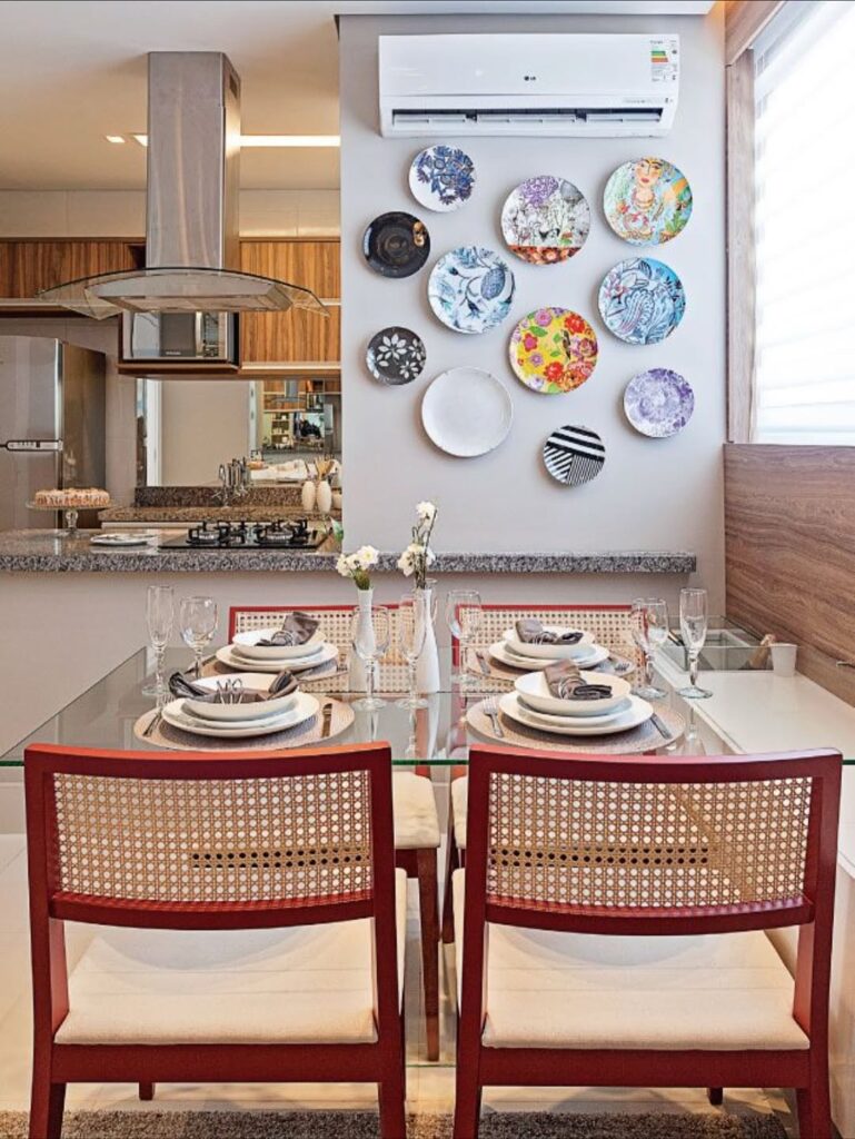 Cozinha com mesa de vidro, cadeiras vermelhas com palhinha e parede decorada com pratod coloridos