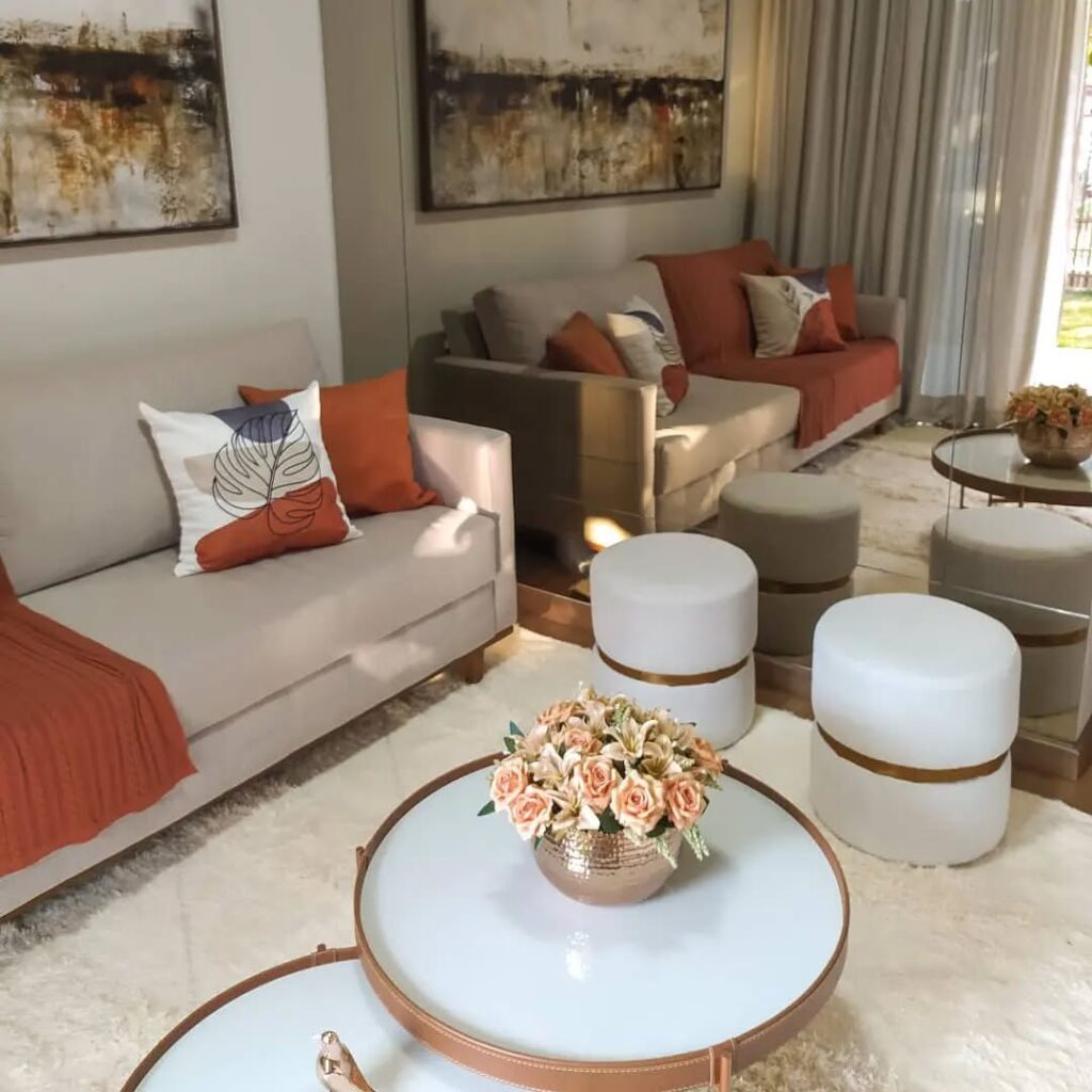Sala de estar com mesas de centro e pufes claros com dourado