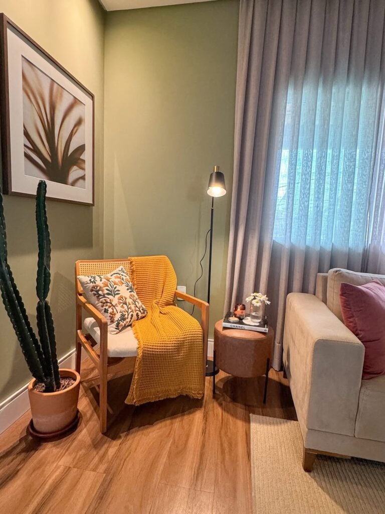 Canto de sala com poltrona de madeira, almofada colorida, manta na cor mostarda, luminária de piso e vaso com cactus