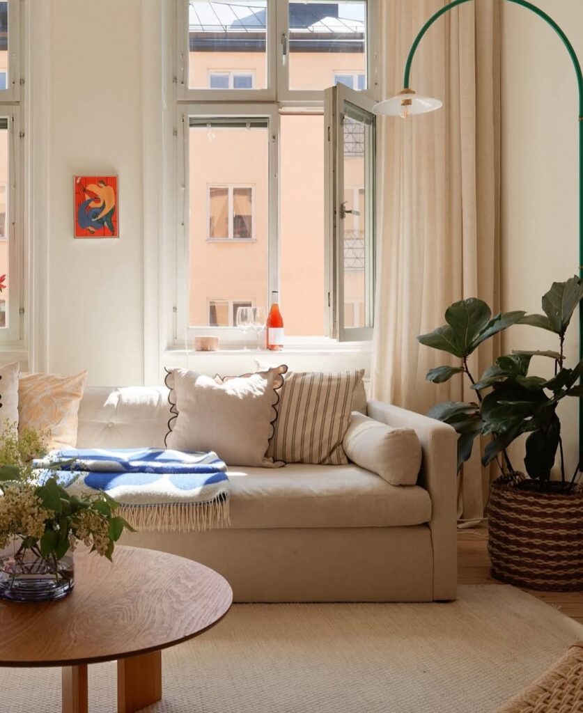 Sala neutra com sofá de linhas retas, cesto com planta, luminária de piso e mesa de centro de madeira