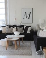 Sala em preto e branco com sofá preto, almofadas com estampas nos tons, mesas de centro com tampo branco e pés de madeira