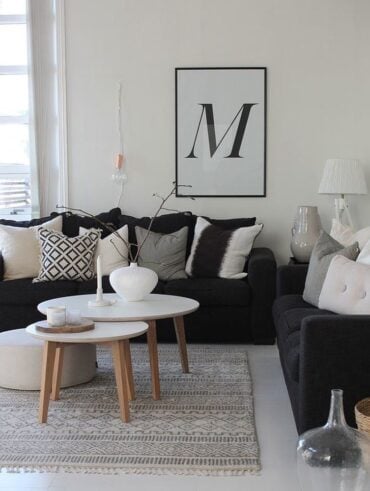 Sala em preto e branco com sofá preto, almofadas com estampas nos tons, mesas de centro com tampo branco e pés de madeira