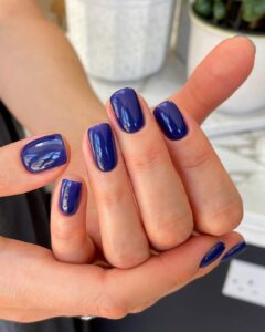 Mãos de pele clara, com unha quadrada azul-marinho
