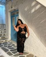 Mulher jovem de pele clara e mid size. Ela usa conjunto de top e saia longa preto.