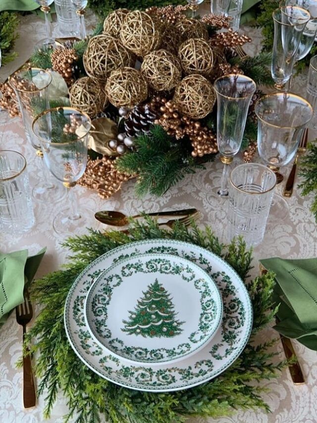 Mesa posta de Natal com pratos brancos decorados com pinheirinhos, taças com bordas douradas e centro de mesa com pinhas e bolas douradas
