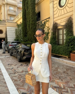Mulher jovem e magra com conjunto de colete e saia curta branco e bolsa de verão