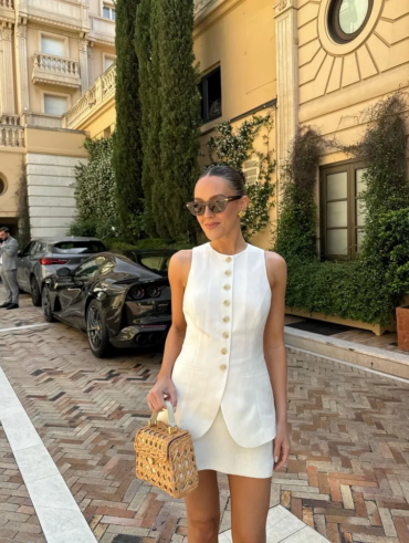 Mulher jovem e magra com conjunto de colete e saia curta branco e bolsa de verão