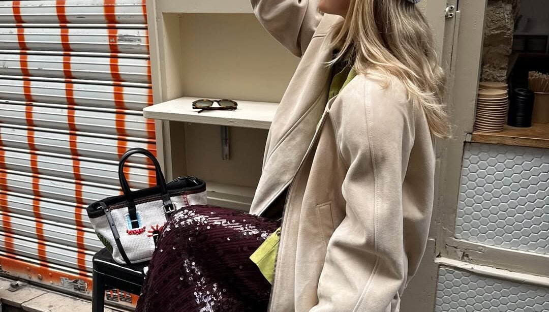 Mulher jovem com jaqueta clara, saia longa de paetê e calçado colorido