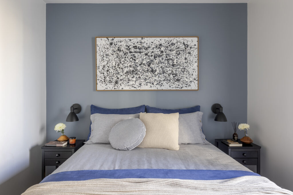Suíte do casal com parede atrás da cama em tom de azul e quadro abstrato
