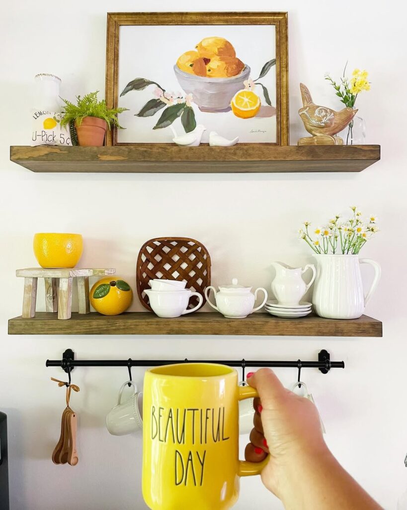 Prateleiras de madeira com louças brancas, elementos amarelos e uma mão de mulher segurando uma caneca amarela