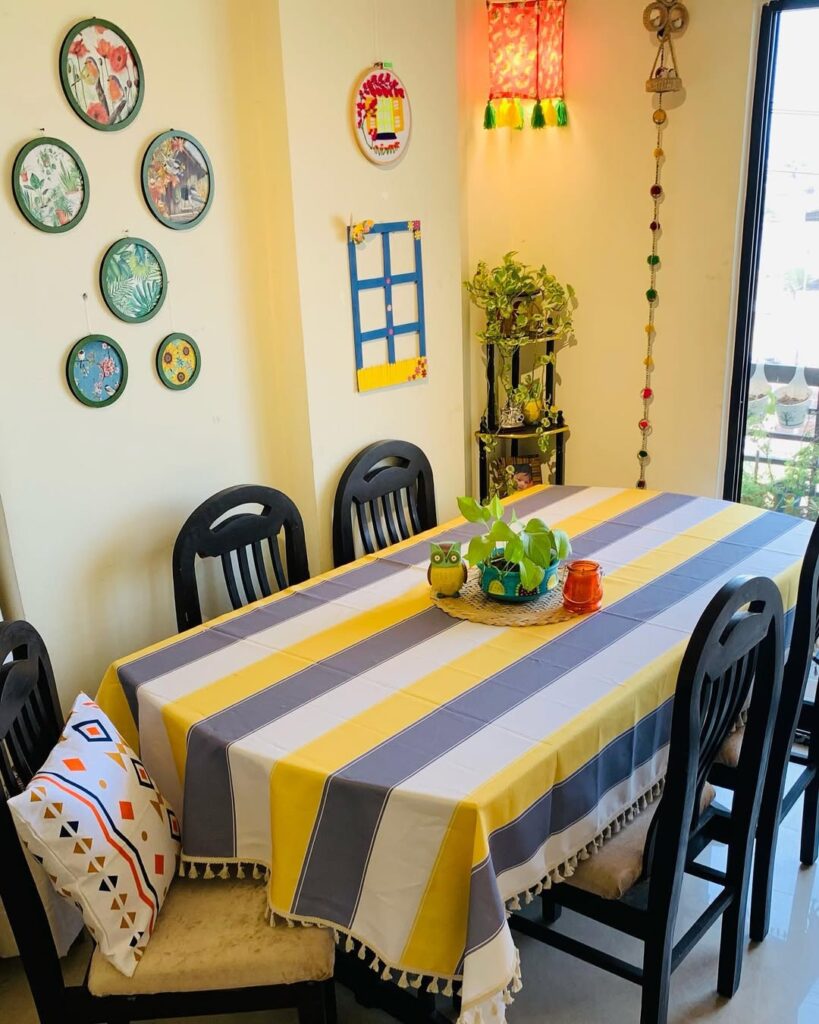 Sala de jantar com toalha listrada em azul, amarelo e branco, e pratos coloridos na parede