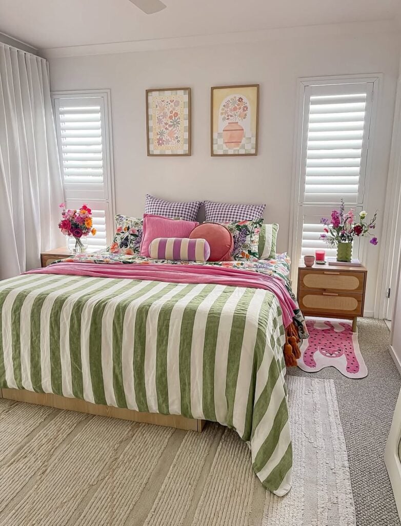 Quarto branco com quadros de flores acima da cabeceira, almofadas coloridas e colcha listrada em verde e branco