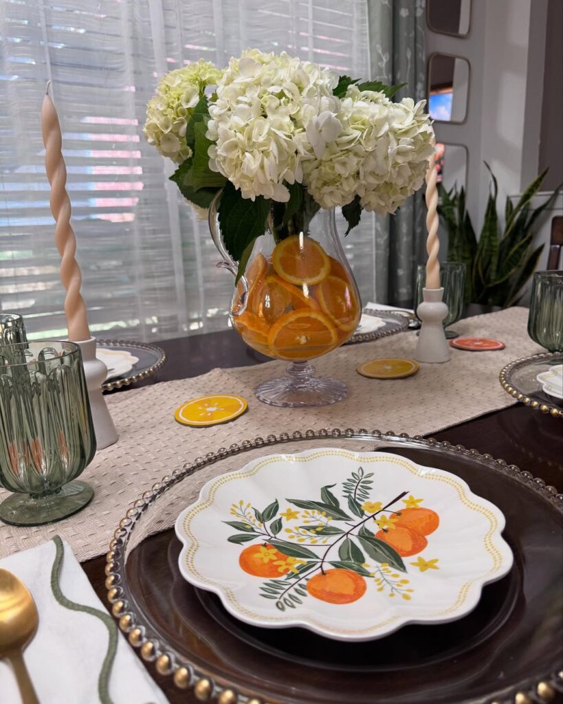 Mesa com prato branco com laranjas desenhadas, vaso com rodelas de laranja e flores brancas