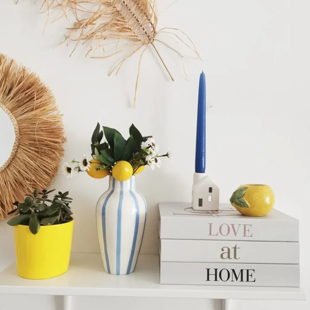 Prateleira com caixas de livros decorativos, vaso branco com listras azuis e vaso amarelo com suculenta