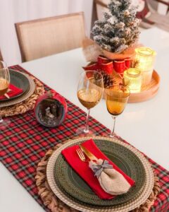 Mesa posta de Natal com bandeja decorada com velas e laço vermelho, caminho de mesa xadrez e pratos verdes