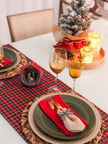 Mesa posta de Natal com bandeja decorada com velas e laço vermelho, caminho de mesa xadrez e pratos verdes