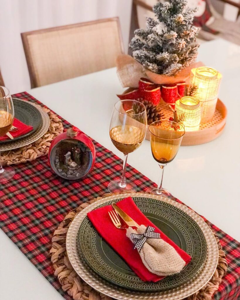 Mesa posta de Natal com bandeja decorada com velas e laço vermelho, caminho de mesa xadrez e pratos verdes