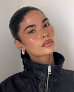 Mulher de pele clara, com jaqueta preta, cabelo preso e maquiagem clean