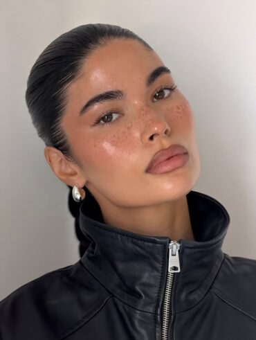 Mulher de pele clara, com jaqueta preta, cabelo preso e maquiagem clean