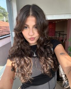 Mulher de pele clara, com blusa preta e cabelo ondulado escuro