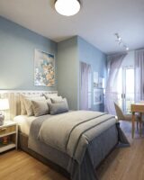 Quarto azul-claro com mesa de cabeceira branca, quadro com flores e edredom cinza