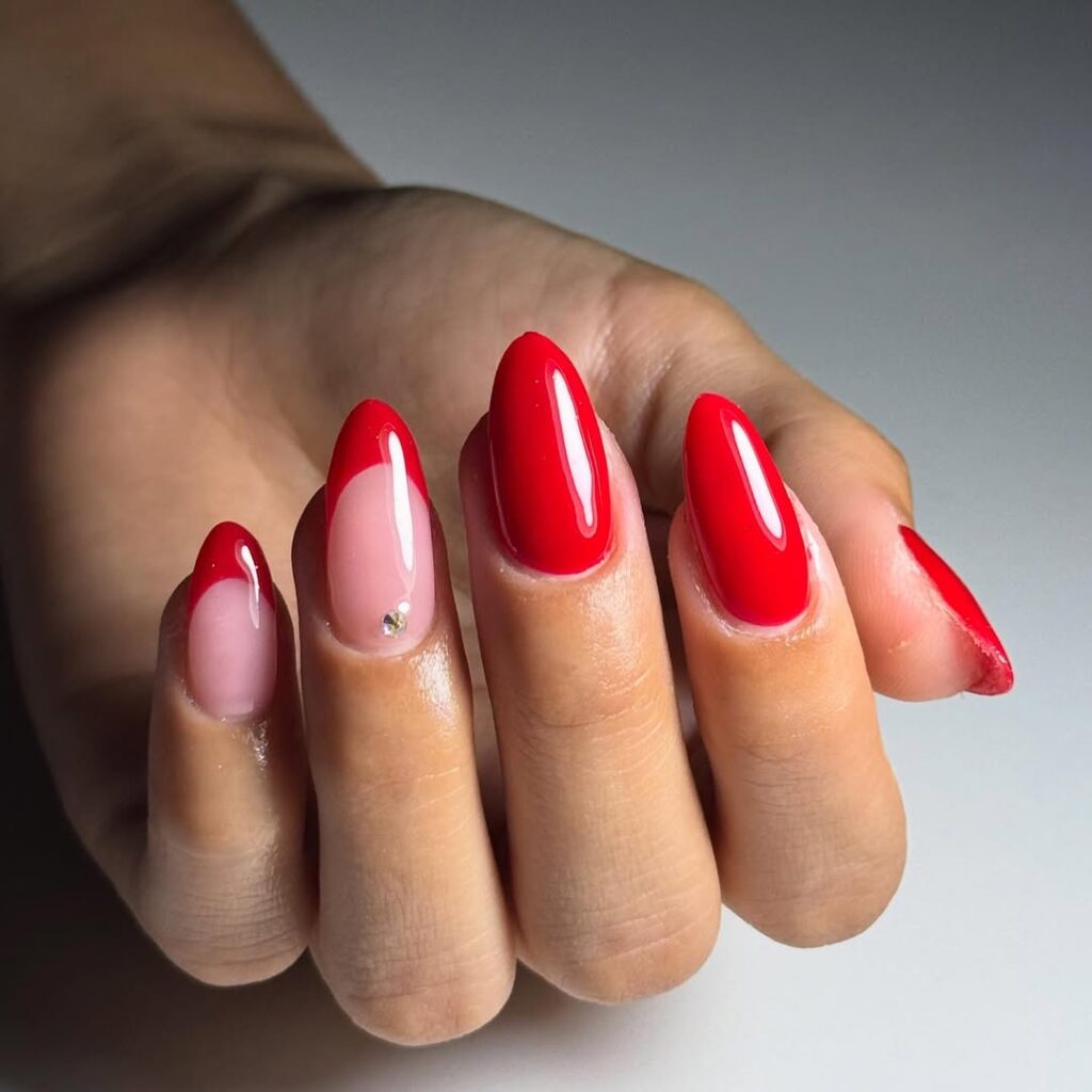 Mão de pele clara, com unha amendoada vermelha com francesinha e strass