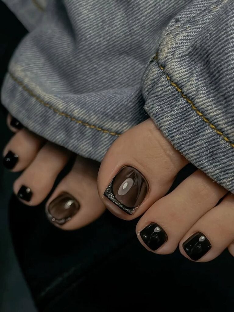 Pés de pele clara, com unhas dos pés pintadas com esmalte preto e decoradas 