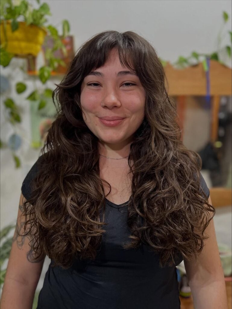 Mulher de pele clara, com cabelo ondulado e franja cortininha 