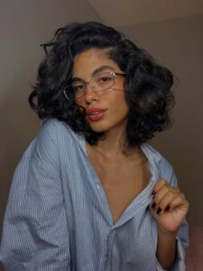 Mulher de pele clara, com blusa listrada, óculos e cabelo ondulado bob