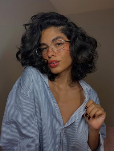 Mulher de pele clara, com blusa listrada, óculos e cabelo ondulado bob