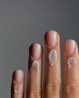 Mão de pele clara, com unha curta neutra e creme nas cutículas