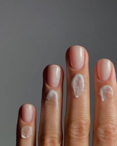 Mão de pele clara, com unha curta neutra e creme nas cutículas
