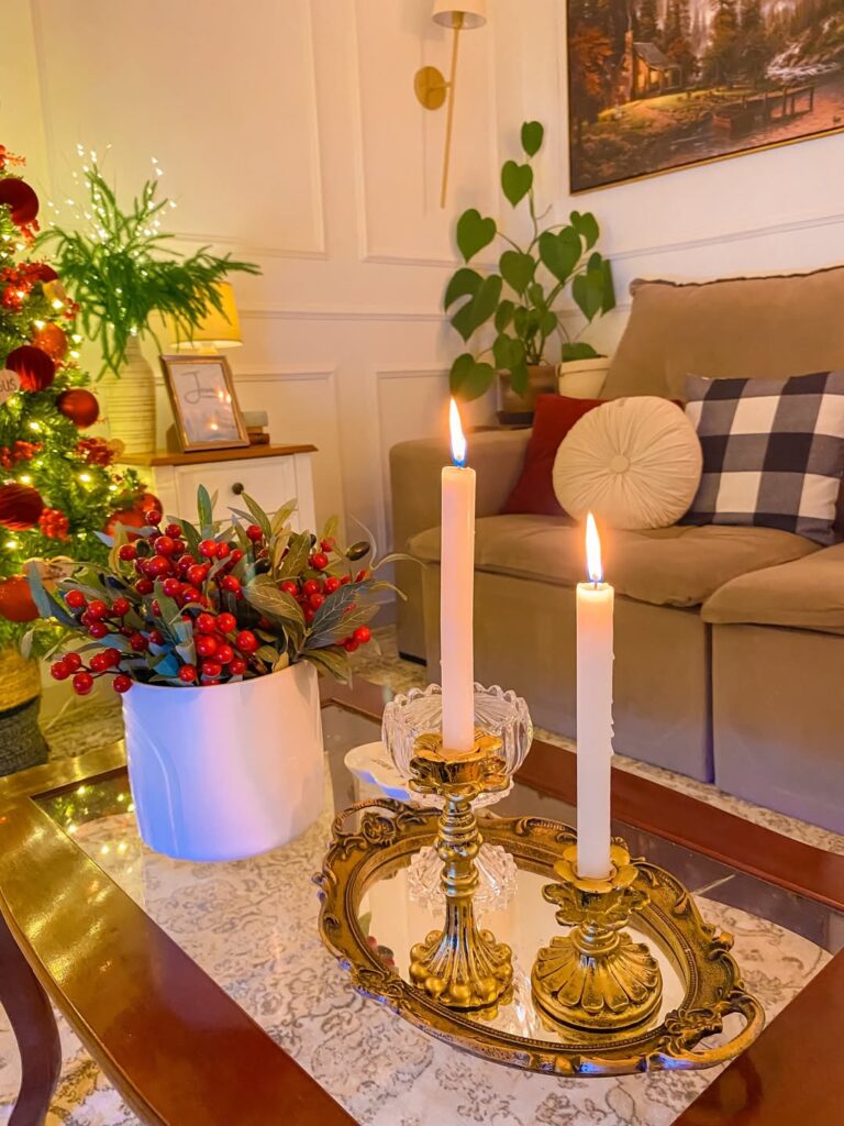 Mesa de centro com vaso branco e azevinhos, bandeja dourada ornamentada com castiçais e velas