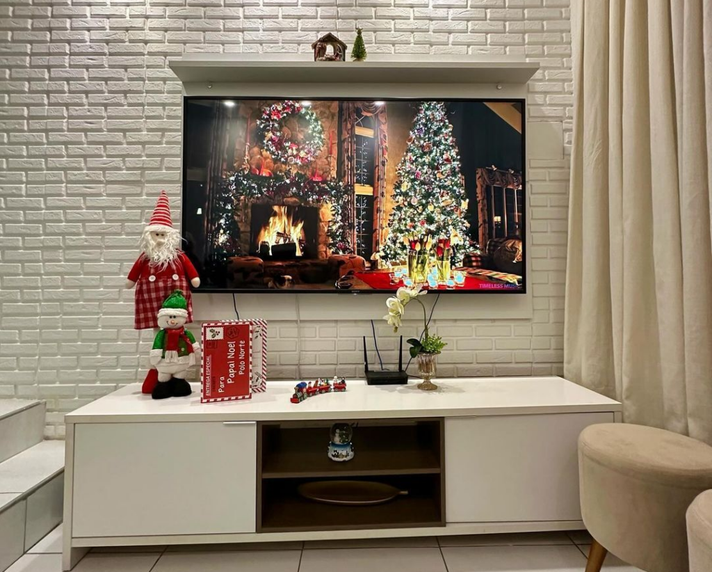 Sala de estar com rack de tv branco, Papai Noel, ajudante e enfeites natalinos