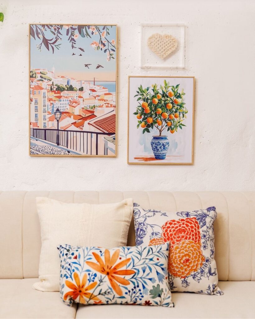 Sofá bege com almofadas coloridas e quadros com paisagem e frutas na parede