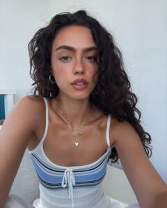 Mulher de pele clara, com regata listrada e cabelo cacheado escuro
