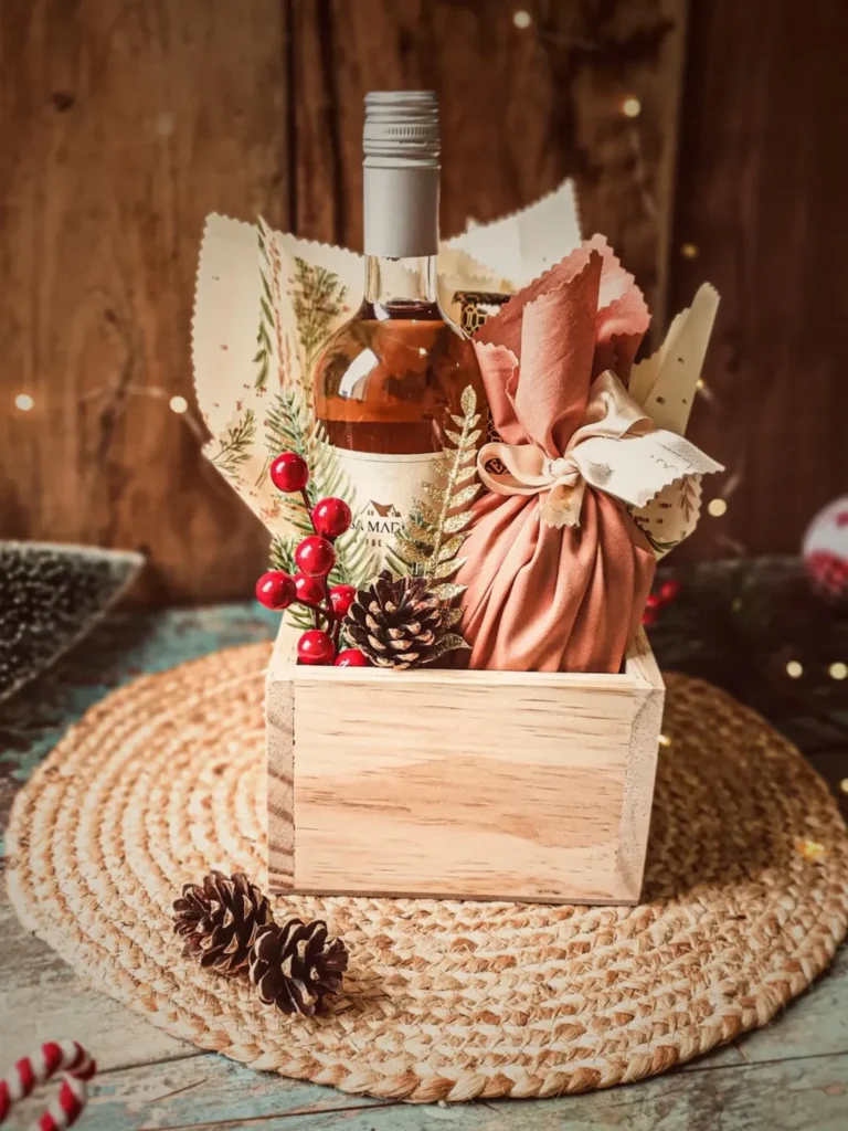 Caixinha de madeira com garrafa de vinho, pinha, azevinhos e um embrulho em tecido rosa