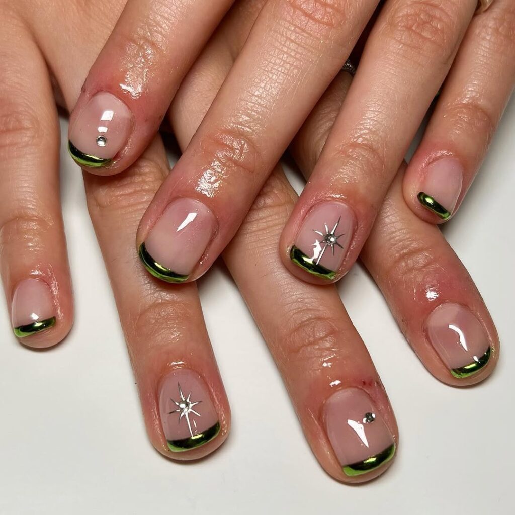 Mão de pele clara, com unha curtinha neutra com francesinha verde metalizada e decorações com estrelas