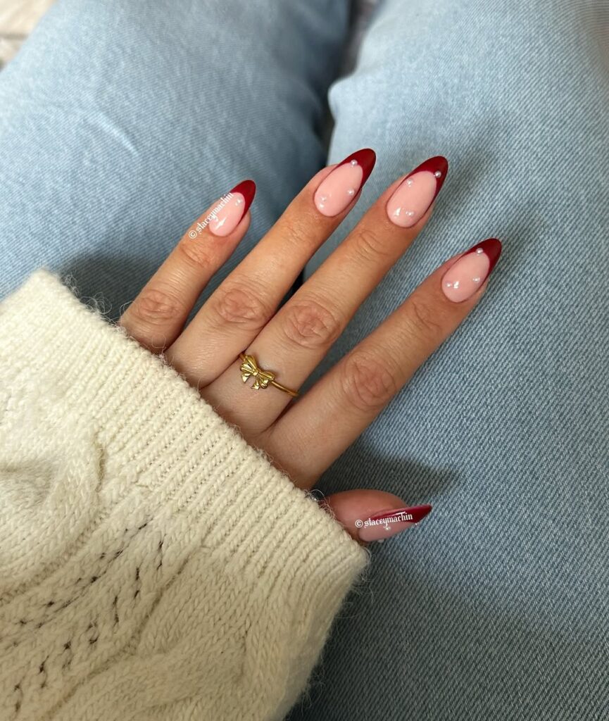 Mão de pele clara, com anel dourado e unha amendoada com francesinha vermelha de decoração com pérolas