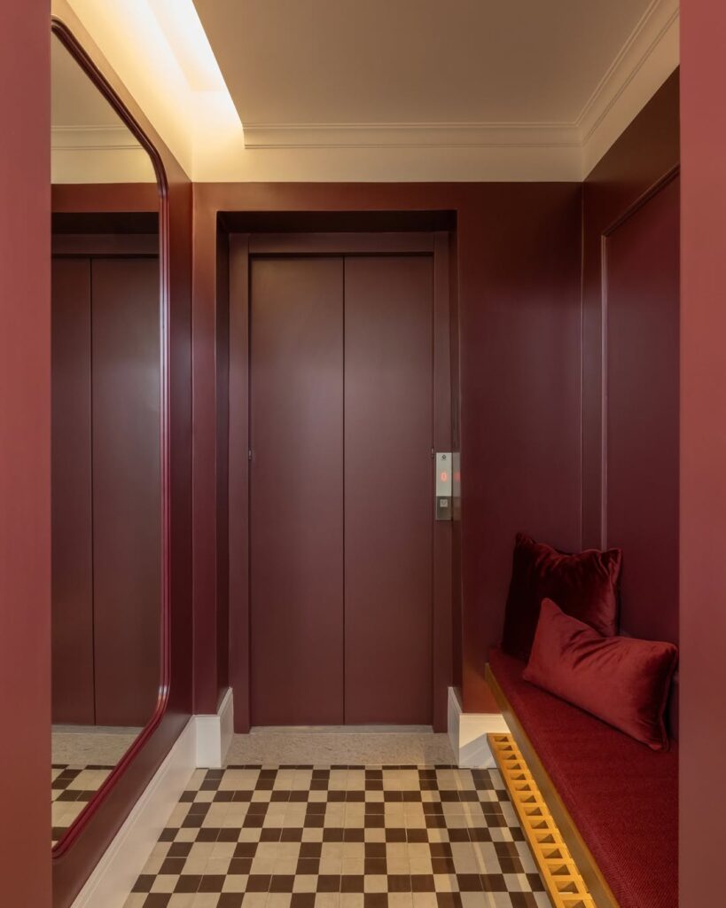 Hall de entrada monocromático bordô, com banco, almofadas e espaço para calçados