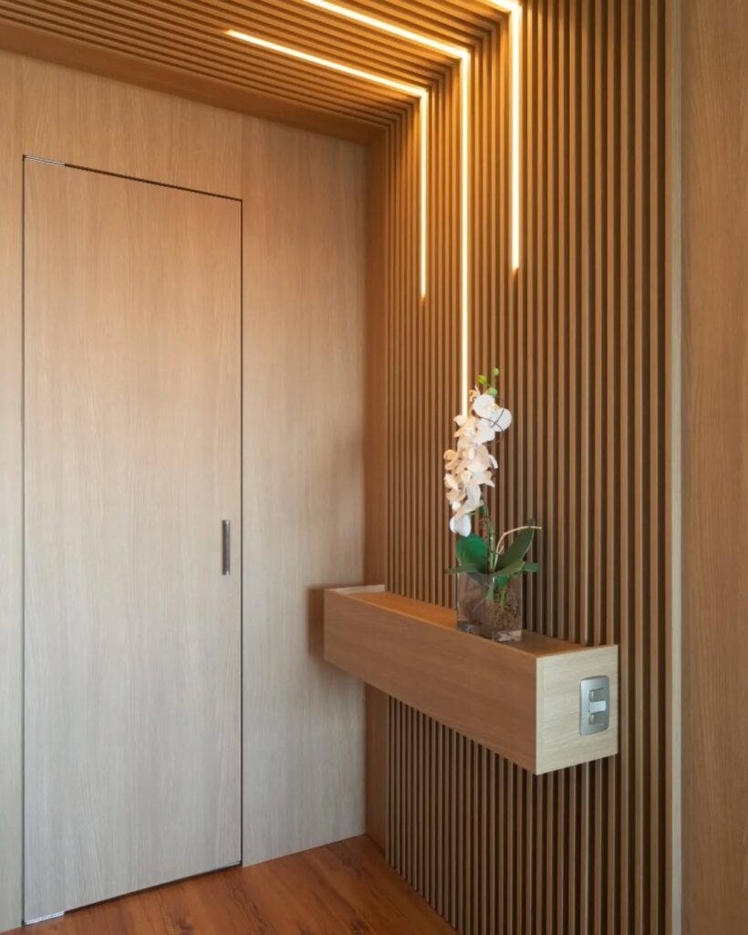 Entrada de apartamento com ripado na parede e no teto, luzes de led, aparador suspenso com orquídea