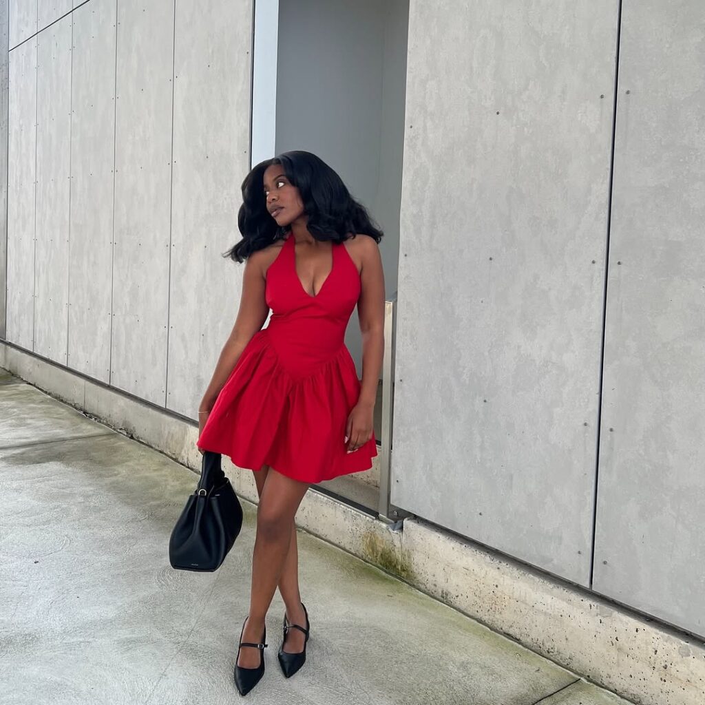 Mulher jovem usando vestido vermelho rodado com sandália preta e bolsa preta